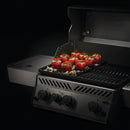 Stuffed tomatoes with herbs and cheese rest atop the Napoleon Enameled Cast Iron Reversible Griddle for Rogue® 425 by Napoleon Grills, shown on a grill with three knobs and a partially opened lid against a dark background.