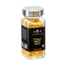 A glass jar of The Spice Lab Organic Minced Garlic, featuring a sleek silver lid and a black label, contains flavorful dried minced garlic pieces—ideal for enhancing avocado toast or any of your favorite dishes. Net weight: 2.4 oz (68g).