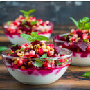 Three glass bowls of yogurt topped with diced beets, pomegranate seeds, The Spice Lab Organic Pine Nuts (a delicious baking ingredient and salad topping from The Spice Lab), and fresh mint leaves, arranged on a wooden surface.