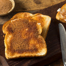 Two slices of toasted bread topped with The Spice Lab Organic Ground Vietnamese Saigon Cinnamon sugar rest on a wooden cutting board, alongside a butter knife and a small bowl filled with more of The Spice Lab’s cinnamon sugar blend.