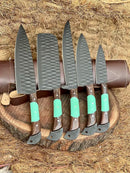 The Texan Knives Premium Knife Set features 13" forged stainless steel blades and wenge wood & resin handles, beautifully displayed on a round wooden board with a leather sheath and straw backdrop.