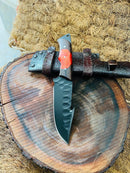 The Texan Knives Hunting Skinning Knife features a 10" J2 steel blade and a wangi/resin handle. It comes with a leather sheath, displayed on rustic wood, perfect for hunters seeking handmade quality and style.