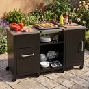 The DirectDeals Outdoor Grill Table 59″ with Removable Shelves & Storage holds drinks, condiments, veggies, meat, and skewers on top. Open shelves store plates and utensils. The wheeled cart is set on a stone patio amidst greenery.