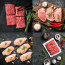 The Dude Food Essentials Meat Box by Dude Food features four types of raw meats—flat iron steaks, pork chops, boneless chicken breasts, and ground beef—each beautifully garnished with herbs and surrounded by seasonings on dark surfaces.
