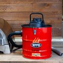 A red WPPO LLC Direct 18V Rechargeable Ash Vacuum With Bonus Value Pack, featuring a black lid and hose attachment, sits on a wood counter. The metal tube is placed next to it, with a wood wall and part of a metal appliance in the background. This rechargeable ash vacuum includes a HEPA filter for efficient and thorough cleaning.