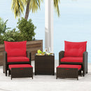 The DirectDeals 5 Pieces Patio Rattan Furniture with 2 Ottomans and Tempered Glass Coffee Table-Red offers stylish outdoor seating, shown here with plants and a palm tree adding charm in the background.