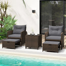 The 5 Pieces Patio Rattan Furniture with 2 Ottomans and Tempered Glass Coffee Table-Red by DirectDeals sits poolside, surrounded by lush plants and a modern building.