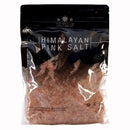 A clear bag labeled The Spice Lab Himalayan Pink Salt Coarse Grain contains coarse grain salt crystals from The Spice Lab, ideal for use in a salt grinder. The packaging features a black top with white text and a transparent lower section that reveals the pink salt inside.