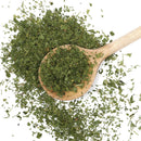 A wooden spoon filled with The Spice Lab Fancy Chervil—dried, chopped green herbs ideal for French cuisine and the delicate flavor of chervil—rests on a white surface, with more of the premium herb from The Spice Lab scattered around it.