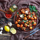 A plate of sautéed mushrooms garnished with parsley sits on a rustic wooden table, surrounded by lemon slices, pepper, utensils, a bottle of oil, and The Spice Lab Organic Smoked Paprika from The Spice Lab. The addition of this organic smoked paprika lends a smoky-sweet flavor that transforms the dish into an irresistible savory delight.