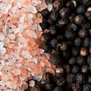 Close-up of The Spice Lab Himalayan Pink Salt and Premium Black Pepper from The Spice Lab Grinder Set, with pink salt crystals and whole peppercorns displayed on a dark surface.