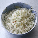 A blue and white bowl filled with cooked white rice, garnished with dried green herbs from The Spice Lab Flavors of Provence Seasoning Set, rests on a light gray surface—an ideal accent for French and Italian-inspired dishes.