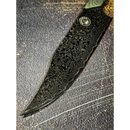 A close-up of the Spaceman Knives Gravity Series Chef Knife shows its AUS-10 steel blade with intricate Damascus patterns, lying on a textured surface marked by visible scratches.