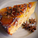 A slice of cake topped with caramelized fruit, powdered sugar, and The Spice Lab Ground Star Anise from The Spice Lab lends an aromatic spice to the dish, adding subtle licorice-like notes, served on a plate.