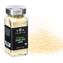 A glass jar from The Spice Lab Organic Starter Spice Set - 6 Jars stands next to a small mound of granulated onion powder on a white background—an essential addition to any starter spice collection for your everyday cooking needs.
