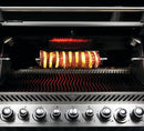 The Napoleon Grills Commercial Grade Rotisserie Kit for Charcoal PRO Grill PRO605CSS (69331) turns skewers of meat and pineapple over hot coals, with control knobs below for precise cooking.