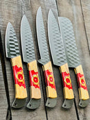 Five Texan Knives Stainless Steel Knife Set 13", featuring forged blades and olivewood & epoxy handles with red and yellow designs, are arranged side by side on a rustic wooden surface.