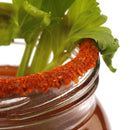 A close-up of a glass rim coated with The Spice Lab Bloody Mary Salt Cocktail Rimmer by The Spice Lab, filled with a savory cocktail and garnished with fresh celery leaves.