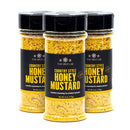 Three jars of The Spice Lab Country Style Honey Mustard Seasoning, each with black lids and visible yellow seasoning inside, featuring labels that highlight it as the perfect honey mustard blend for chicken and pork. This country style BBQ seasoning from The Spice Lab adds delicious flavor to your favorite dishes.