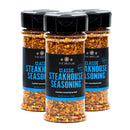 Three bottles of The Spice Lab Classic Steakhouse Steak Seasoning, featuring black lids and blue labels, are arranged in a triangular formation on a white background, highlighting the ideal steak seasoning from The Spice Lab for all your grilling needs.