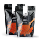 Two black pouches of The Spice Lab Sweet Rib Rub by The Spice Lab, a flavorful Low Sodium BBQ Rub, are shown with a wooden spoon and spilled seasoning on the packages. Each pouch is labeled Net Wt. 2 lb—making them an ideal choice for anyone looking for bulk BBQ spices.