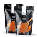 Two black resealable bags labeled The Spice Lab Smoky Pecan Rub by The Spice Lab, each featuring an image of orange-brown seasoning and a wooden spoon on the front—a versatile sweet and smoky BBQ seasoning that also serves as a flavorful smoky pecan rub for grilling or roasting.