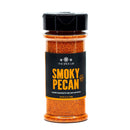 A clear plastic spice jar with a black lid holds The Spice Lab Smoky Pecan Rub, featuring a reddish-brown blend inside. The label highlights its sweet and smoky flavor and recommends the rub for beef, pork, and chicken.