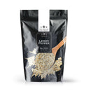 A black resealable bag of The Spice Lab Lemon Pepper Seasoning sits with a wooden spoon holding the citrus pepper blend and some sprinkled nearby. The Spice Lab’s branding appears at the top, along with a net weight of 2 lbs, noting its sugar-free seasoning qualities.