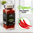 A jar labeled The Spice Lab Organic Chili Powder Blend sits on a counter next to four fresh red chili peppers. In the background, a blurred kitchen appears alongside text that reads The Spice Lab Organic Chili Powder Blend, highlighting it as the perfect organic chili powder for adding authentic Mexican seasoning to your favorite dishes.