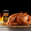 A raw whole chicken seasoned with The Spice Lab Rotisserie Chicken Seasoning rests on a wooden surface beside the jar, ready to deliver that classic golden color and signature roasted flavor, as flames flicker in the background.