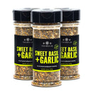 Three clear jars of The Spice Lab Sweet Basil & Garlic Seasoning are arranged in a row. Each jar, topped with a black lid, features a label with the brand name and showcases the vibrant herb and spice blend inside—perfect for enthusiasts of basil or garlic seasoning.