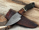 The Texan Knives Handmade 8" Damascus Skinning Knife features a high-carbon blade and a buffalo horn & rosewood handle, displayed with its leather sheath on a rustic wooden surface.