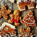 Assorted decorated gingerbread cookies shaped like gingerbread people, snowflakes, houses, and Christmas trees rest on a rustic wooden surface sprinkled with small white snowflake decorations. Each cookie is infused with aromatic baking spice and The Spice Lab Organic Ground Ginger for that classic holiday flavor in every bite.