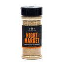 The Spice Lab Night Market Seasoning comes in a clear plastic jar with a black lid, labeled with The Spice Lab brand. Inside is a light brown blend inspired by classic Asian salt and pepper seasoning, perfect for enhancing meat, fish, and poultry.