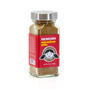 A glass jar with a metal lid contains The Spice Lab Nom Nom Paleo Magic Mushroom Powder, an umami seasoning made with porcini mushrooms. The jar features a red label with a cartoon face and white text displaying the product name from The Spice Lab brand.
