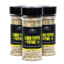 Three clear bottles of The Spice Lab Lemon Pepper + Thyme Seasoning, featuring a vibrant yellow and black seasoning blend, are displayed on a white background.