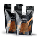 Two black resealable bags of The Spice Lab Cajun Seasoning stand upright, each representing the bold spirit of Louisiana-style flavor. A wooden spoon brimming with this signature Cajun seasoning appears on every package, while accents of brown seasoning are scattered artfully across the bags.