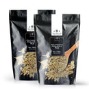 Two black resealable bags of The Spice Lab Polynesian Pineapple Rub, each containing 21 ounces, are displayed with a wooden spoon holding the vibrant spice blend against a white background. Featuring The Spice Lab branding, this tropical seasoning infuses your grilling favorites with a sweet and savory BBQ flavor for an island-inspired twist.