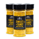 Three bottles of The Spice Lab Sweet + Tangy Mustard Rub, each adorned with a black label and yellow text, are grouped together against a white background. This flavorful seasoning from The Spice Lab is ideal for anyone looking to add a sweet mustard rub or tangy mustard flavor to their favorite dishes.