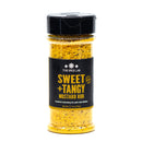 A clear spice jar labeled The Spice Lab Sweet + Tangy Mustard Rub holds vibrant yellow seasoning inside. The label highlights this tangy mustard blend as perfect for pork and chicken. Net weight: 5.7 oz.