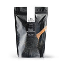 A black resealable pouch labeled The Spice Lab Black Steak Seasoning sits behind a wooden spoon brimming with the bold seasoning, its contents spilling artfully in front of the bag. Crafted by The Spice Lab and infused with activated charcoal, this blend delivers a savory steakhouse flavor that elevates every bite.
