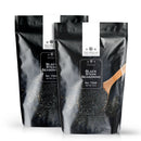 Two black resealable bags of The Spice Lab Black Steak Seasoning are shown, each featuring the brand name at the top. In front of the bags, a wooden spoon holds the seasoning, emphasizing this signature blend crafted with activated charcoal for a bold, savory steakhouse flavor.