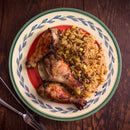 A plate with three roasted chicken drumsticks seasoned with The Spice Lab Whole Thyme by The Spice Lab, served alongside rice mixed with corn and peas on a wooden table next to a fork and knife.