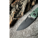 The Spaceman Knives N1 EDC, featuring a green Micarta handle and a matte black 14C28N Sandvik steel blade, rests on rough stone next to rugged tree bark.