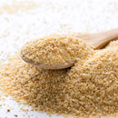 A wooden spoon scoops up a pile of The Spice Lab Organic Minced Garlic on a white surface, with additional dried garlic granules from The Spice Lab scattered around.