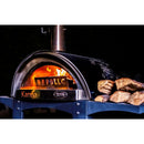 A wood-fired pizza oven labeled Karma, aglow with flames and burning wood, stands against a dark background with logs stacked to the side. Featured in the setup is the WPPO Wood-Fired Oven Flame / Heat Deflector by WPPO LLC Direct—a must-have pizza oven accessory designed to evenly distribute heat throughout the cooking chamber.