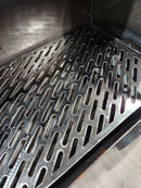 a close-up view of a metal grate or perforated surface, with a pattern of holes or slits arranged in a grid-like pattern.