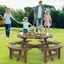 A family with two kids and a dog walks toward the DirectDeals 8-Person Round Picnic Table Set Circular Patio Dining Camping Table with Benches, decorated with cakes, fruit, flowers, and candles on green grass among trees.
