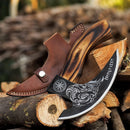 The Texan Knives Custom Hand-Engraved Pizza Axe, featuring an 8-inch J2 steel blade and wooden handle, rests on stacked logs beside its brown leather sheath with stitching and snap button, blurred logs in the background.