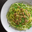 A white plate filled with spiralized zucchini noodles topped with ground meat and green sauce, garnished with chopped fresh herbs and a sprinkle of The Spice Lab Nom Nom Paleo Magic Mushroom Powder by The Spice Lab for an added layer of earthy umami flavor.